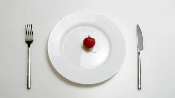 The concept of diet and healthy lifestyle. Top view of a plate in which lies a radish, with a fork and a knife, is on the table. — ストック写真