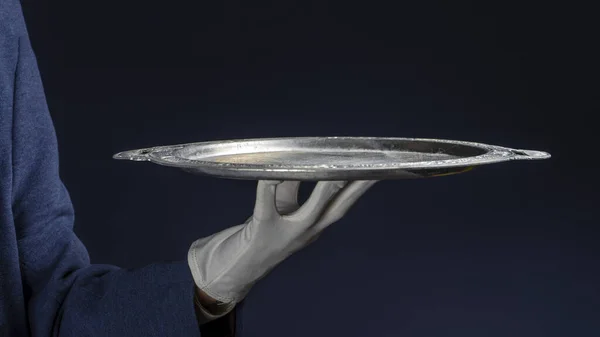 Photo A butler wearing a white glove holding a tray. Black background.