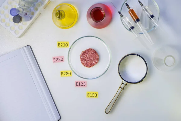 Sağlıklı fotoğraf yeme konsepti. Laboratuvarın masasında bir büyüteç var, bir parça sosis E gıda laboratuarının katkı maddelerinin isimleriyle süslenmiş..