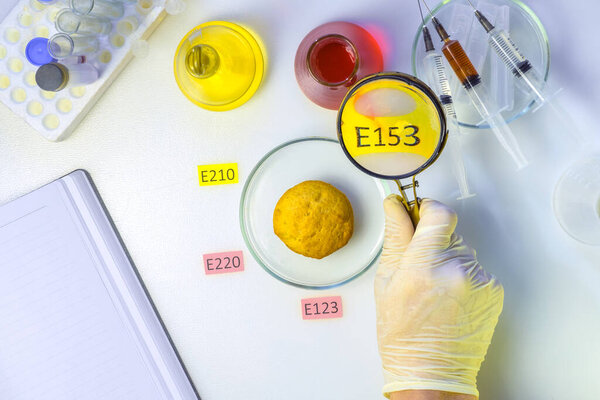 Photo Healthy food concept. The hand of the laboratory assistant is holding a magnifier, a cupcake decorated with tablets with the names of additives E. Food Laboratory.