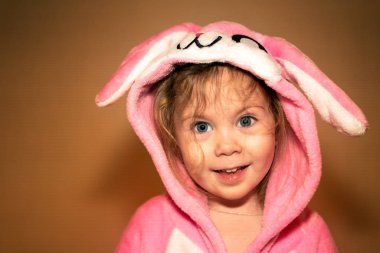 Küçük kız beyaz arka plan üzerinde duran ve çikolata Paskalya yumurtaları tutan Paskalya tavşanı gibi giyinmiş.