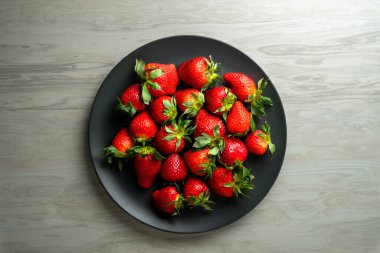 Siyah tabakta taze çilekler, siyah ahşap arka planda.