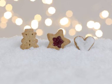 Beyaz kar üzerinde renkli Noel kurabiyeleri ve arka planda parlayan ışıklar. 