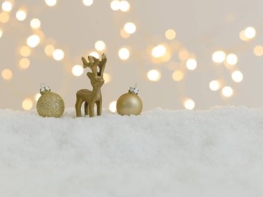 Beyaz kar üzerinde altın noel eşyaları ve arka planda parlak ışıklar.