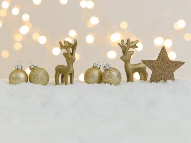 Beyaz kar üzerinde altın noel eşyaları ve arka planda parlak ışıklar.