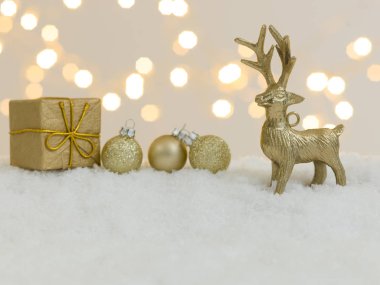 Beyaz kar üzerinde altın noel eşyaları ve arka planda parlak ışıklar.