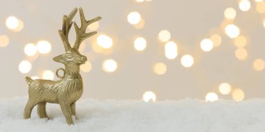 Beyaz kar üzerinde altın yılbaşı geyiği ve arka planda parlak ışıklar.