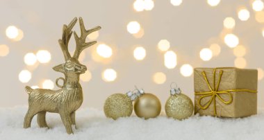 Beyaz kar üzerinde altın noel eşyaları ve arka planda parlak ışıklar.