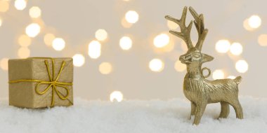 Beyaz kar üzerinde altın noel eşyaları ve arka planda parlak ışıklar.