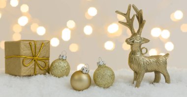 Beyaz kar üzerinde altın noel eşyaları ve arka planda parlak ışıklar.