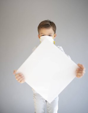 7 yaşında koruyucu maske takan ve elinde boş beyaz tabela tutan bir çocuk.