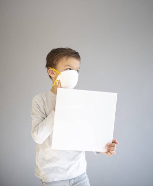 7 yaşında koruyucu maske takan ve elinde boş beyaz tabela tutan bir çocuk.