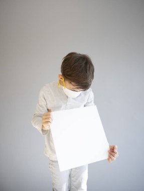 7 yaşında koruyucu maske takan ve elinde boş beyaz tabela tutan bir çocuk.