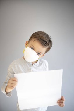7 yaşında koruyucu maske takan ve elinde boş beyaz tabela tutan bir çocuk.