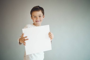 Gri arka planda beyaz çarşaf tutan havalı genç çocuk. 