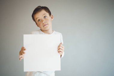 Gri arka planda beyaz çarşaf tutan havalı genç çocuk. 