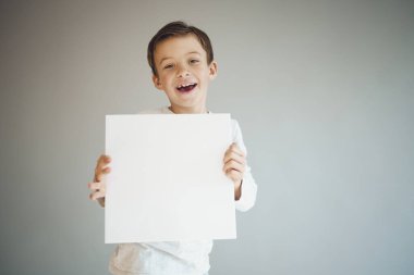 Gri arka planda beyaz çarşaf tutan havalı genç çocuk. 