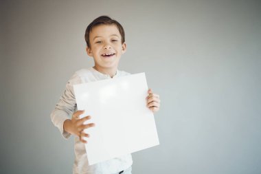 Gri arka planda beyaz çarşaf tutan havalı genç çocuk. 