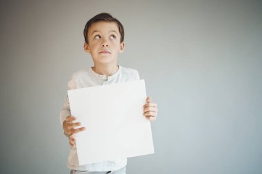 Gri arka planda beyaz çarşaf tutan havalı genç çocuk. 