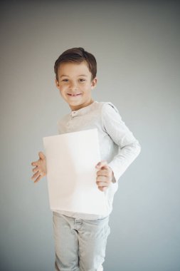 Gri arka planda beyaz çarşaf tutan havalı genç çocuk. 