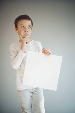 Gri arka planda beyaz çarşaf tutan havalı genç çocuk. 