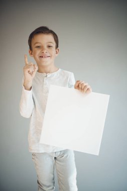 Gri arka planda beyaz çarşaf tutan havalı genç çocuk. 