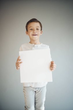 Gri arka planda beyaz çarşaf tutan havalı genç çocuk. 