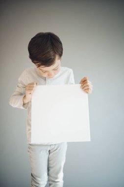 Gri arka planda beyaz çarşaf tutan havalı genç çocuk. 