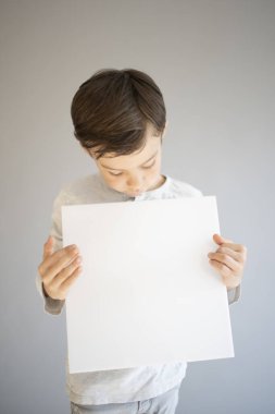 Gri arka planda beyaz çarşaf tutan havalı genç çocuk. 