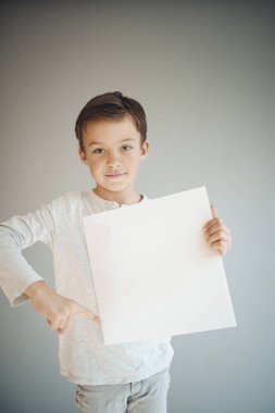 Gri arka planda beyaz çarşaf tutan havalı genç çocuk. 