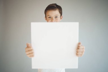 Gri arka planda beyaz çarşaf tutan havalı genç çocuk. 