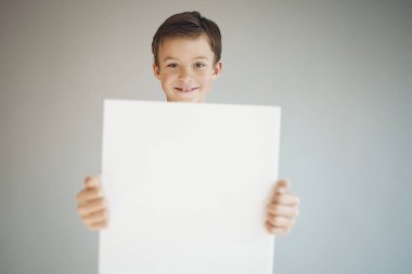 Gri arka planda beyaz çarşaf tutan havalı genç çocuk. 