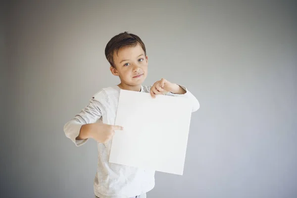 Крутой Мальчик Держащий Белый Пустой Лист Перед Серым Фоном — стоковое фото