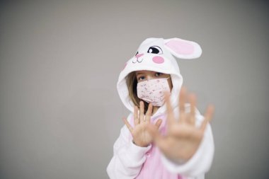 Paskalya tavşanı kostümlü güzel bir kız ve gri arka planda koruyucu bir maskeyle poz veriyor. Coronavirus tecridi sırasında paskalya konsepti. 