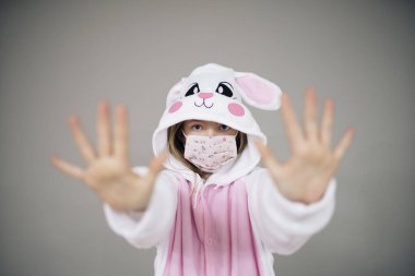 Paskalya tavşanı kostümlü güzel bir kız ve gri arka planda koruyucu bir maskeyle poz veriyor. Coronavirus tecridi sırasında paskalya konsepti. 