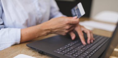 İş kadınının evde laptopu ve kredi kartıyla alışveriş yaparken çekilmiş görüntüsü mutfak masasında.