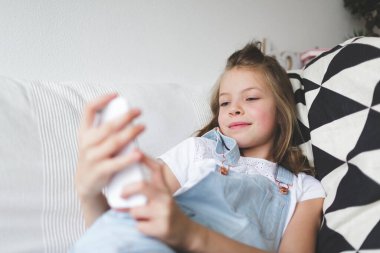Kanepede akıllı telefonlu genç bir kız Corona krizi sırasında video görüşmesi yapıyor.