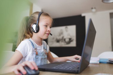 Kulaklıklı güzel bir genç kız karantina sırasında dizüstü bilgisayarla çalışıyor.