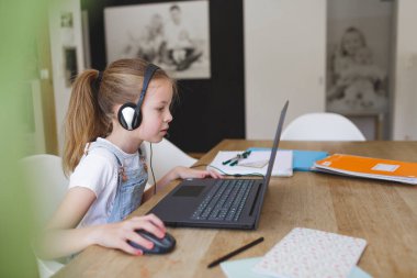 Kulaklıklı güzel bir genç kız karantina sırasında dizüstü bilgisayarla çalışıyor.