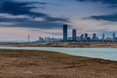 Sıcak, güneşli bir günde güzel, beyaz, kumlu bir plajın üzerinde modern, metropoliten bir şehir kulesinin uzun gökdelenleri..