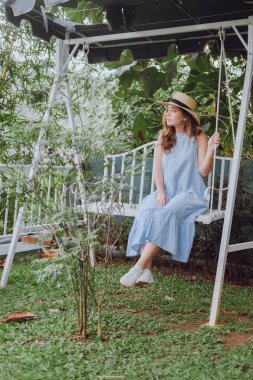 Şapkalı bir genç kadın bir salıncağa oturur