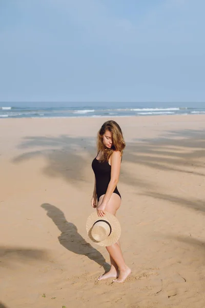 Dívka v černých plavkách a klobouku chůzi na pláži — Stock fotografie