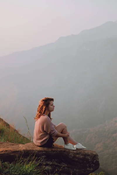 La niña se sienta en una piedra con una vista de las montañas — Foto de Stock