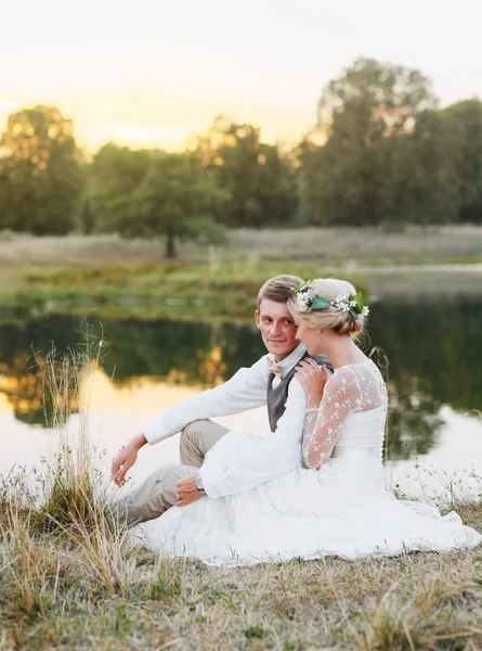 Just married loving hipster couple in wedding dress and suit on green field in a forest at sunset. happy bride and groom sitting in the summer meadow. Romantic Married young family. — Stock Photo, Image