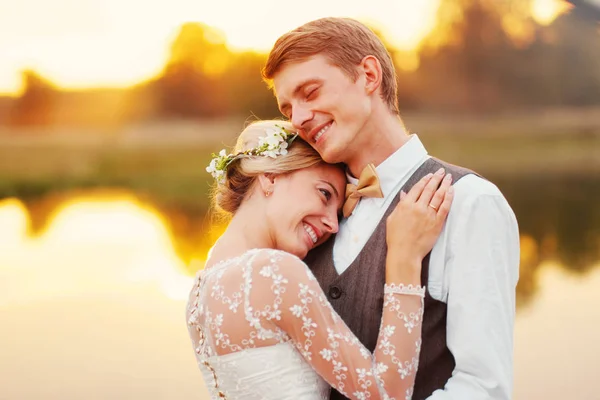 Bruden och brudgummen står vid sjön efter vigseln. Nygifta leende, de är glada. Foto i varm toning. — Stockfoto