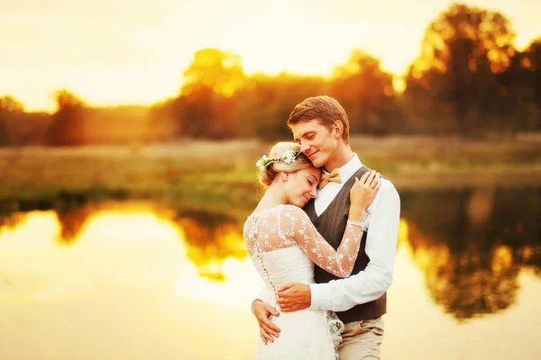 Narzeczeni stać nad jeziorem, po ceremonii ślubnej. Nowożeńcy są uśmiechnięte, są szczęśliwi. Zdjęcie w ciepłe zabarwienie. — Zdjęcie stockowe