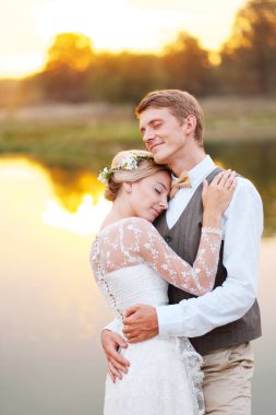 Yeni evliler birbirlerine günbatımında gölde sarılıyorlar. Ağaçlar ve gökyüzü göl yansıtır