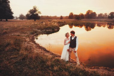 Gelin ve damat göl arka planı kırmızı günbatımı poz. Genel planı