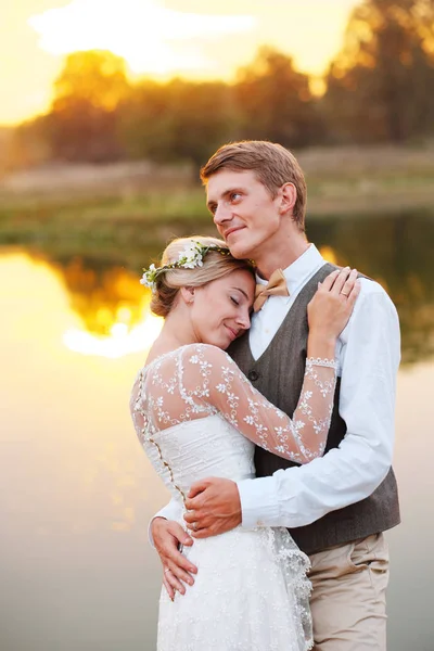 Os recém-casados ficam em frente a um lago ao pôr-do-sol — Fotografia de Stock