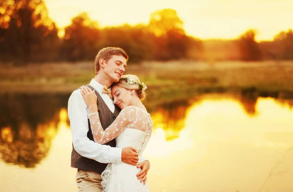 Nowożeńcy, przytulanie siebie na tle czerwony zachód słońca — Zdjęcie stockowe
